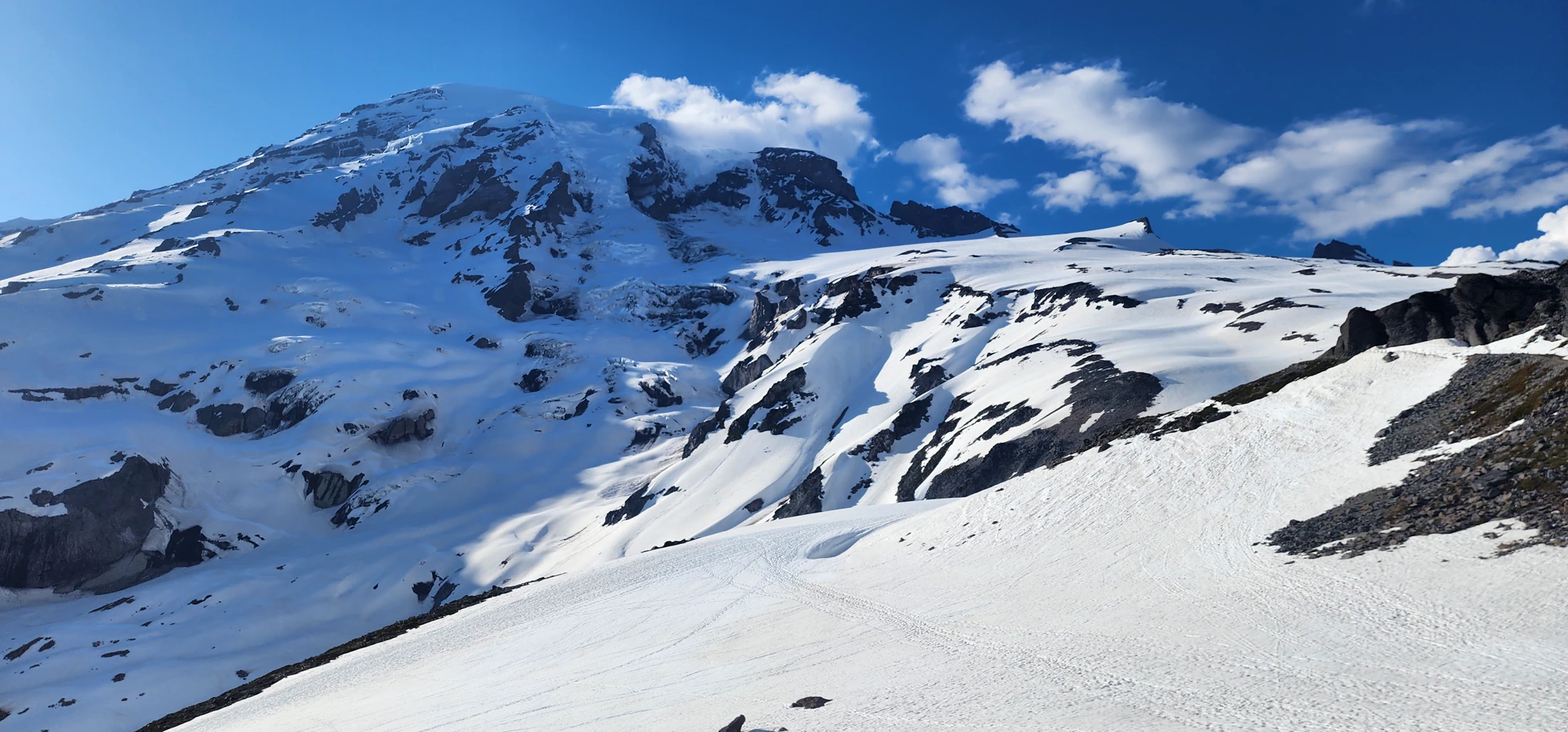 A close view of snow-covered Mount Rainier beneath a deep blue sky and drifting clouds.